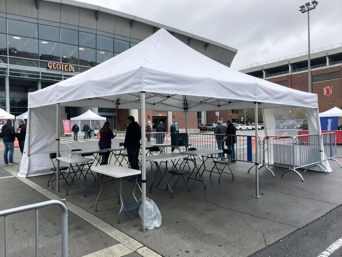 White event tent with tables and crowd barriers set up outside an arena entrance