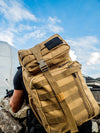Picture of Cobra tactical sling backpack, desert colour, in tactical action on someone’s back. A black and white US flag is attached on the top outer pouch, to the right. 