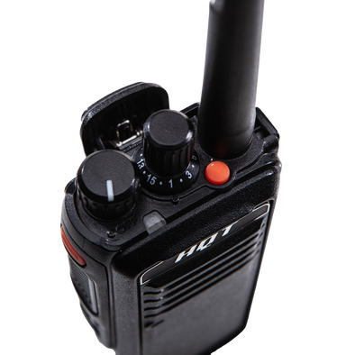 Picture of a black radio from a top, front-left side controls angle, with the back clip-on sticking out. The top of has a left on/off-volume button, followed by a 16 channels selection button, and an antenna cut by the picture, and at the front of the top, an LED light and a red top key. The front top displays the HQT brand. The left side shows the top side key and the push-to-talk key.