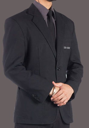 Man wearing a single-breasted black blazer with notched collar, over a grey dress shirt with black tie. Genesis logo embroidered on the left chest pocket in light grey.