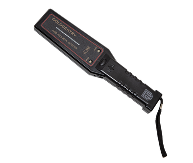 Picture of the flat control surface of a black, hand-held security metal detector, crossing diagonally form the top left to the bottom right corner, a black wrist strap hanging vertically to the right of the shaft edge. The upper half coil surface is wider than the lower half and its LED signal indicator bar and two LED spotlights, signals for readiness and alert, are framed by a red contour line. The shaft has a manual emission button at the edge of the control surface, followed by the alert sound trigger.