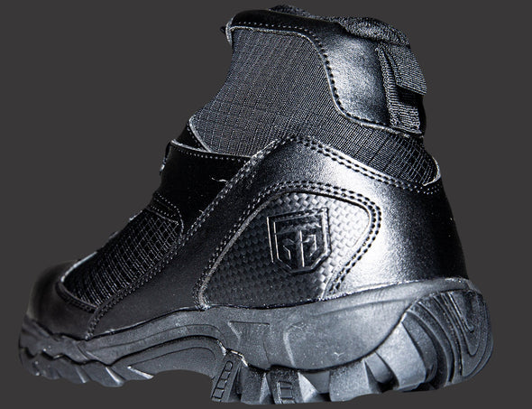 Picture from an outside-back angle of a left, ankle height, fully black boot. The boot displays the inch-high outsole, topped by the intricate combination of leather and mesh fabric of the boot, with pull tab at the top, and embossed with the GTG logo at the heel to the right.